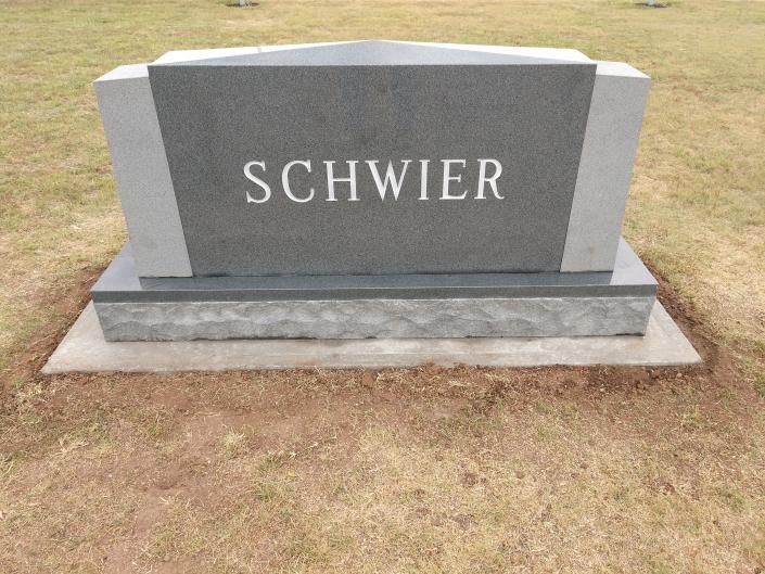 Gray granite gravestone with the name “SCHWIER” in a grassy cemetery area