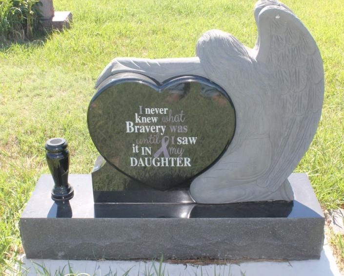 Gray memorial gravestone with engraved heart and angel wings in a grassy cemetery