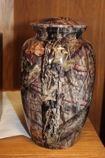 Camouflage-patterned ceramic vase on a wooden shelf against a wood-paneled background