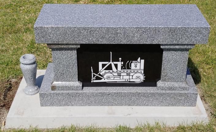 Gray stone memorial with a black inset plaque featuring a white construction truck illustration
