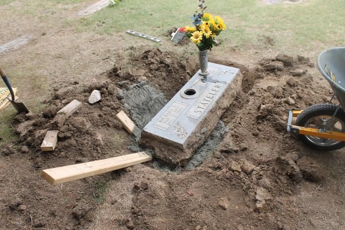 Grave marker with flowers at a freshly dug cemetery plot, soil piled around it
