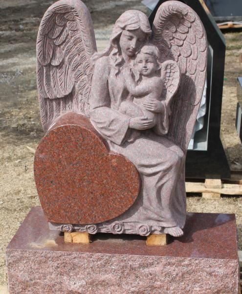 Stone angel statue with wings holding a child, partially covered by a red heart-shaped plaque.