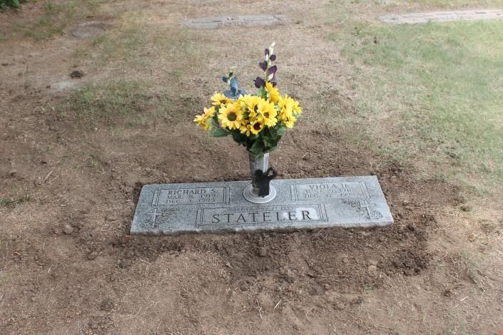 Grave marker with yellow flowers in a cemetery plot on bare ground