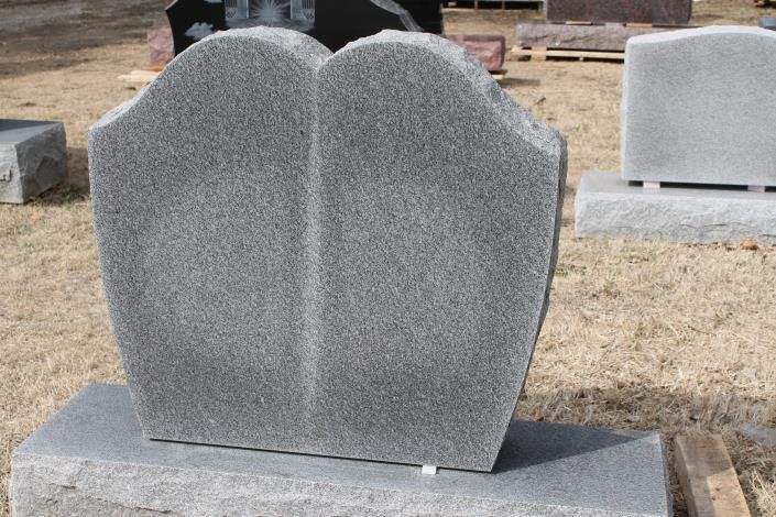 Gray granite double-headstone on a cemetery plot, with a curved top and split center.