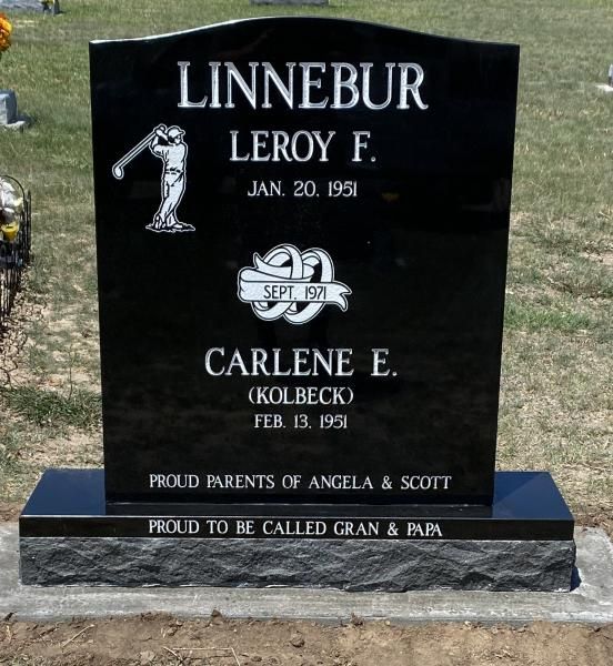 Black granite gravestone with engraved names and dates in a cemetery.