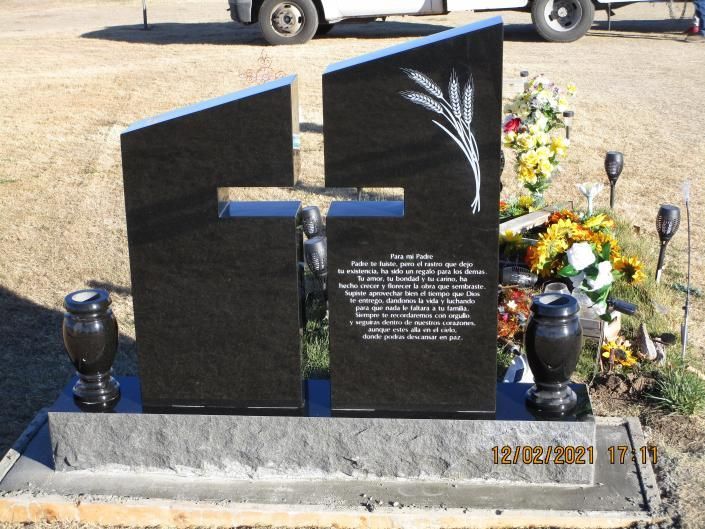 Black memorial headstone with cross, flowers, and lanterns at a gravesite