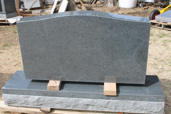 Gray granite headstone on a wooden pallet in an outdoor stone yard