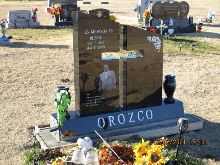 Memorial gravestone with flowers and a blue base reading OROZCO in a cemetery during daylight