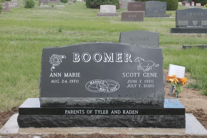 Two black gravestones in a cemetery, one marked “Boomer,” with flowers beside them.