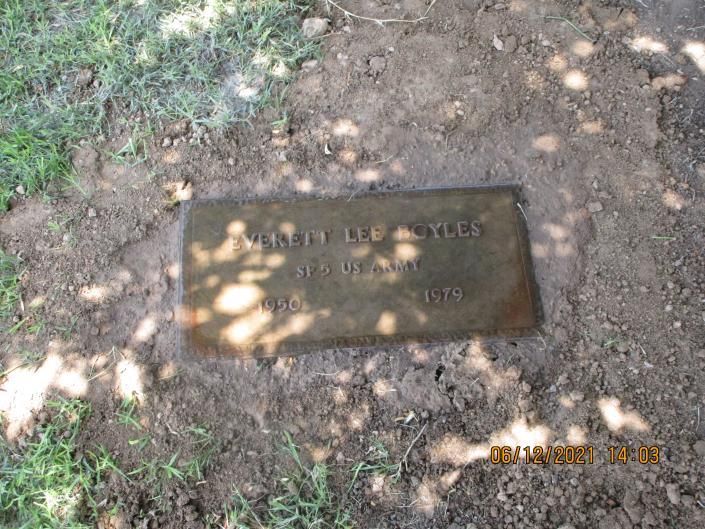 Small brass plaque set in dirt under dappled sunlight beside grass.