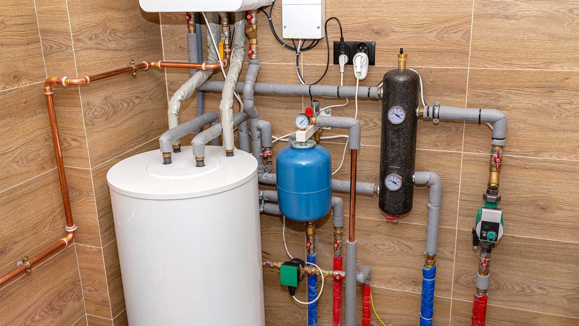 A water heater is sitting in a room surrounded by pipes.