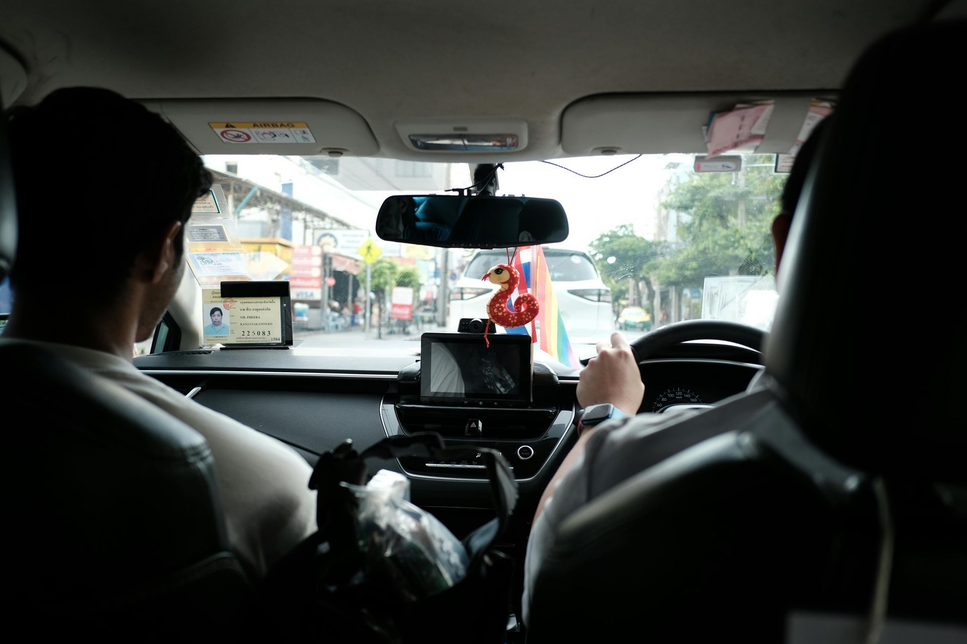 Interior view of a car with two people in the front seats, driving on a road.