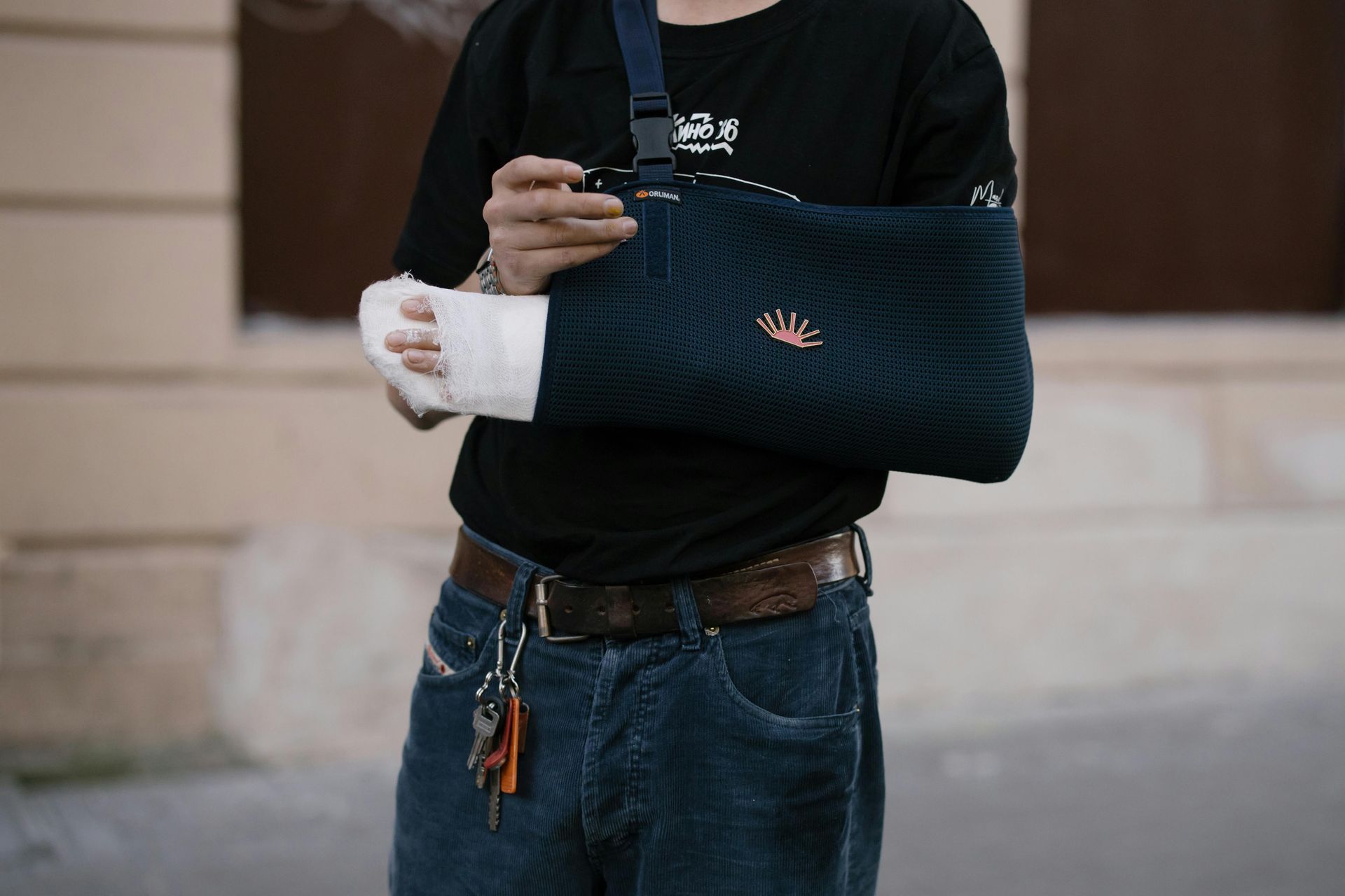 Person with a cast on their arm, wearing a black shirt and jeans, holding arm in a sling.