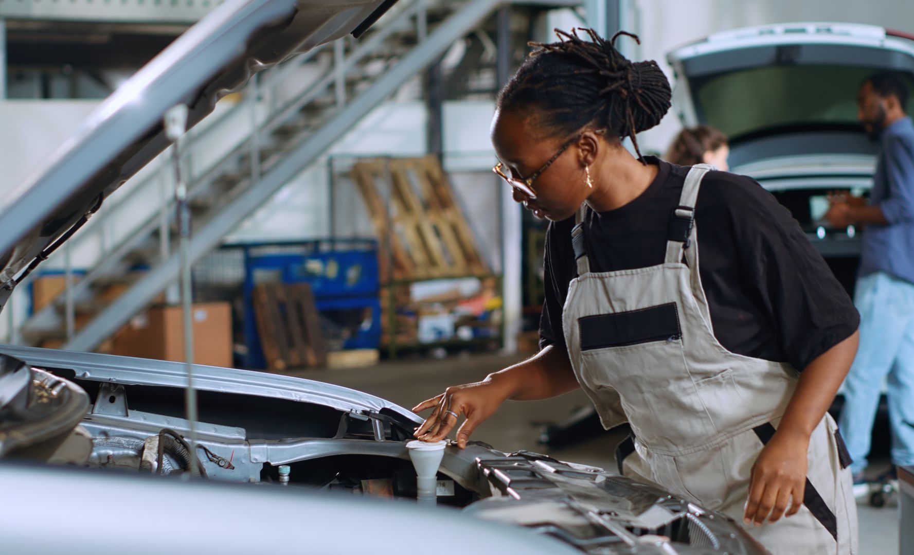 Black woman mechanic checking fluids under car hood in a garage.