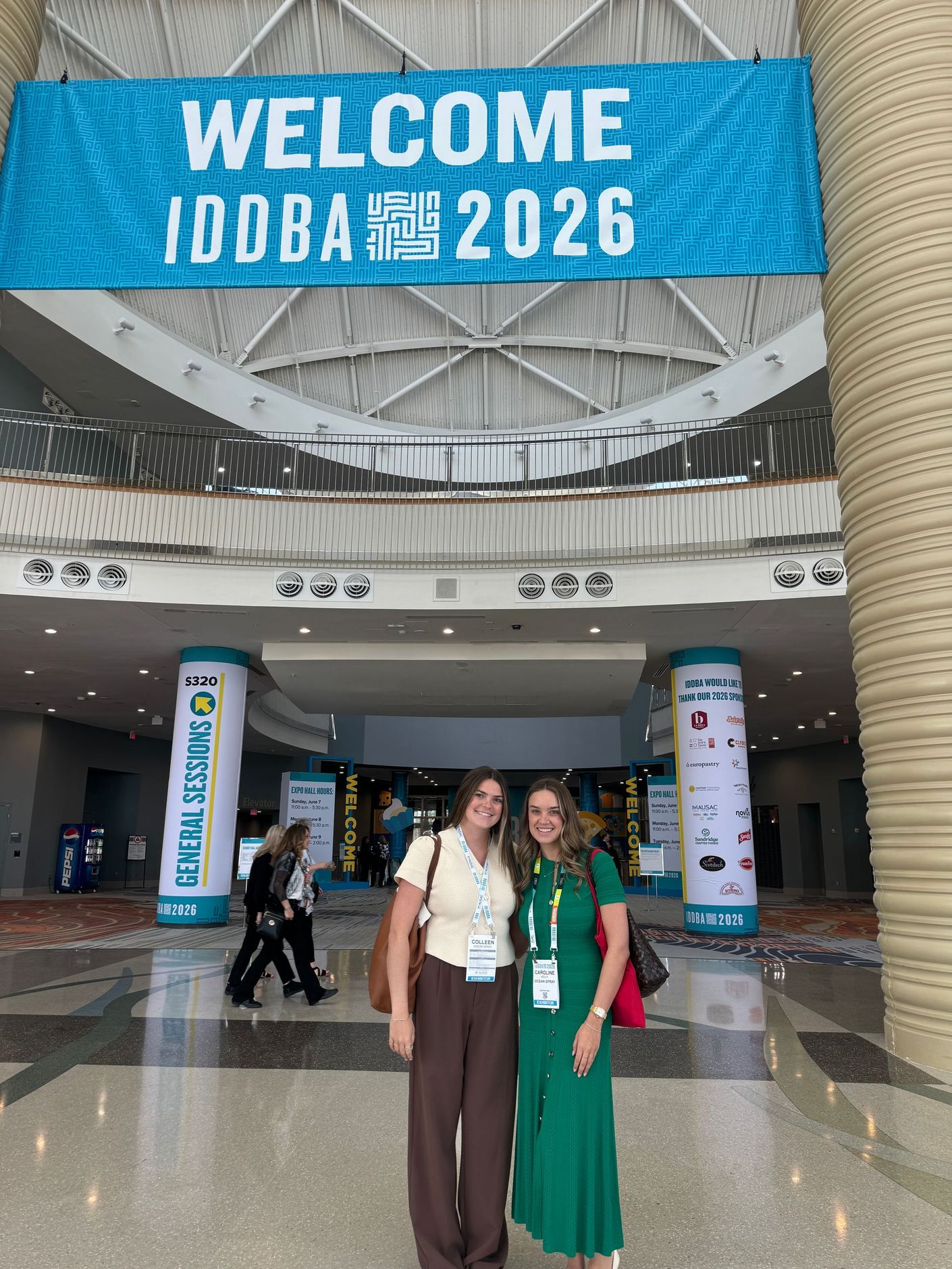Two women posing in a convention lobby beneath a large “WELCOME IODBA 2026” banner