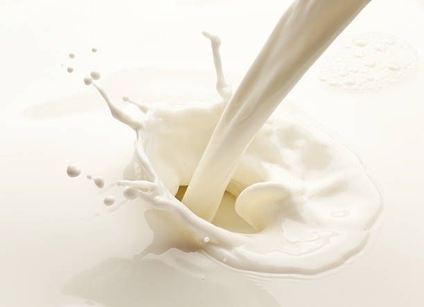 Milk is being poured into a glass on a white surface
