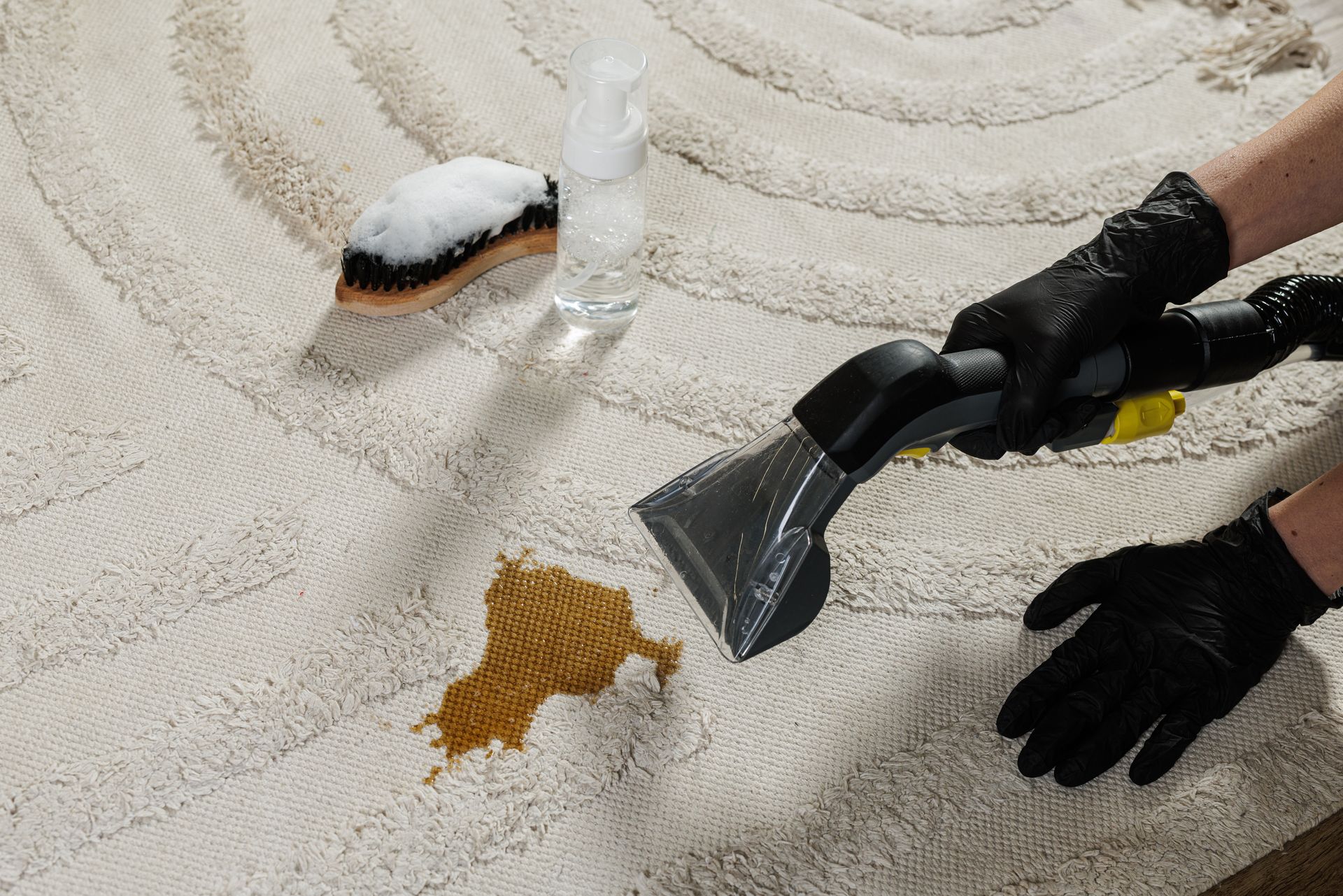 Technician removing a stain from carpet using a cleaning tool, with a brush and spray bottle nearby