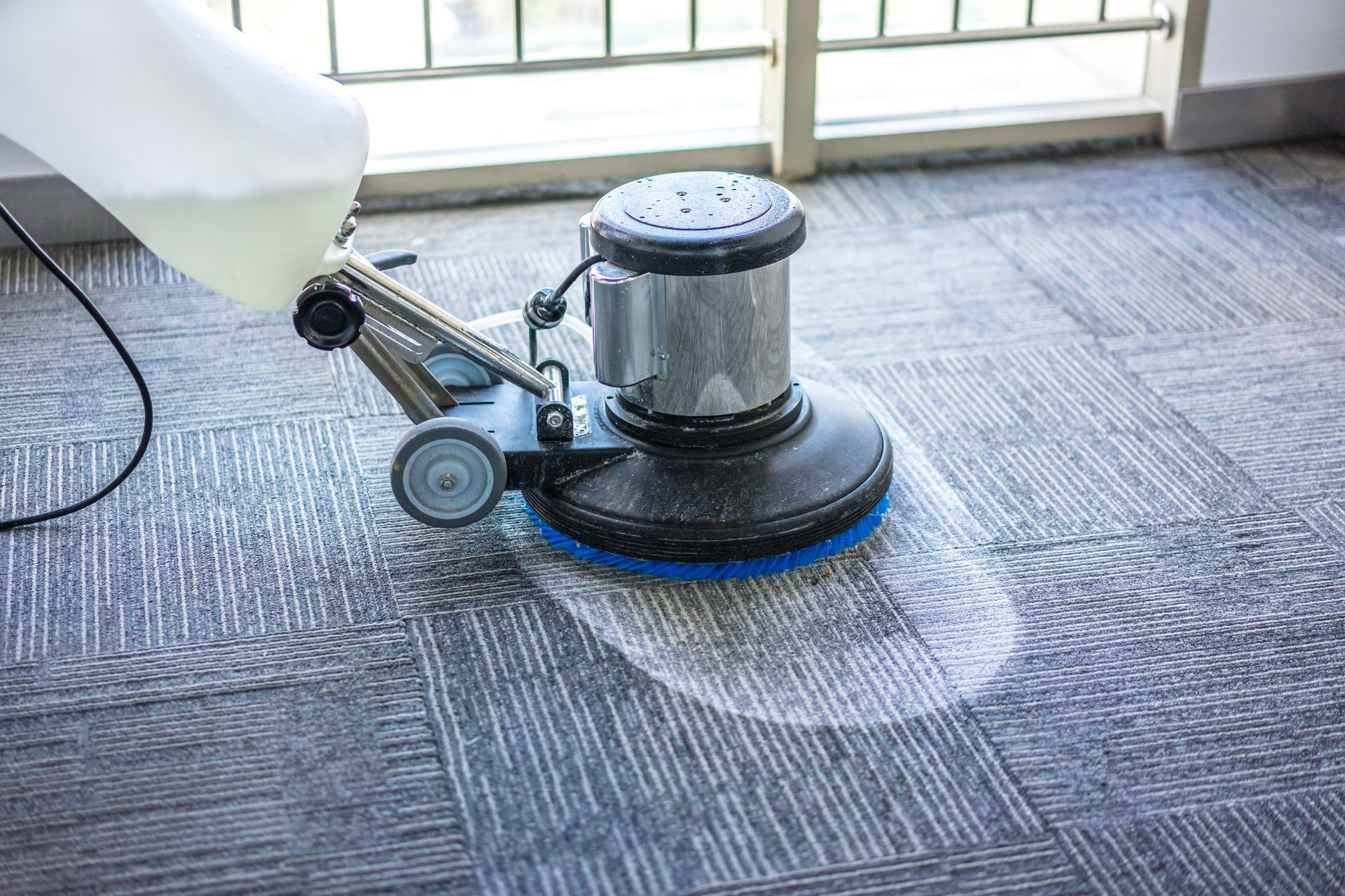 Commercial rotary carpet cleaning machine with foam treatment on office carpet tiles.