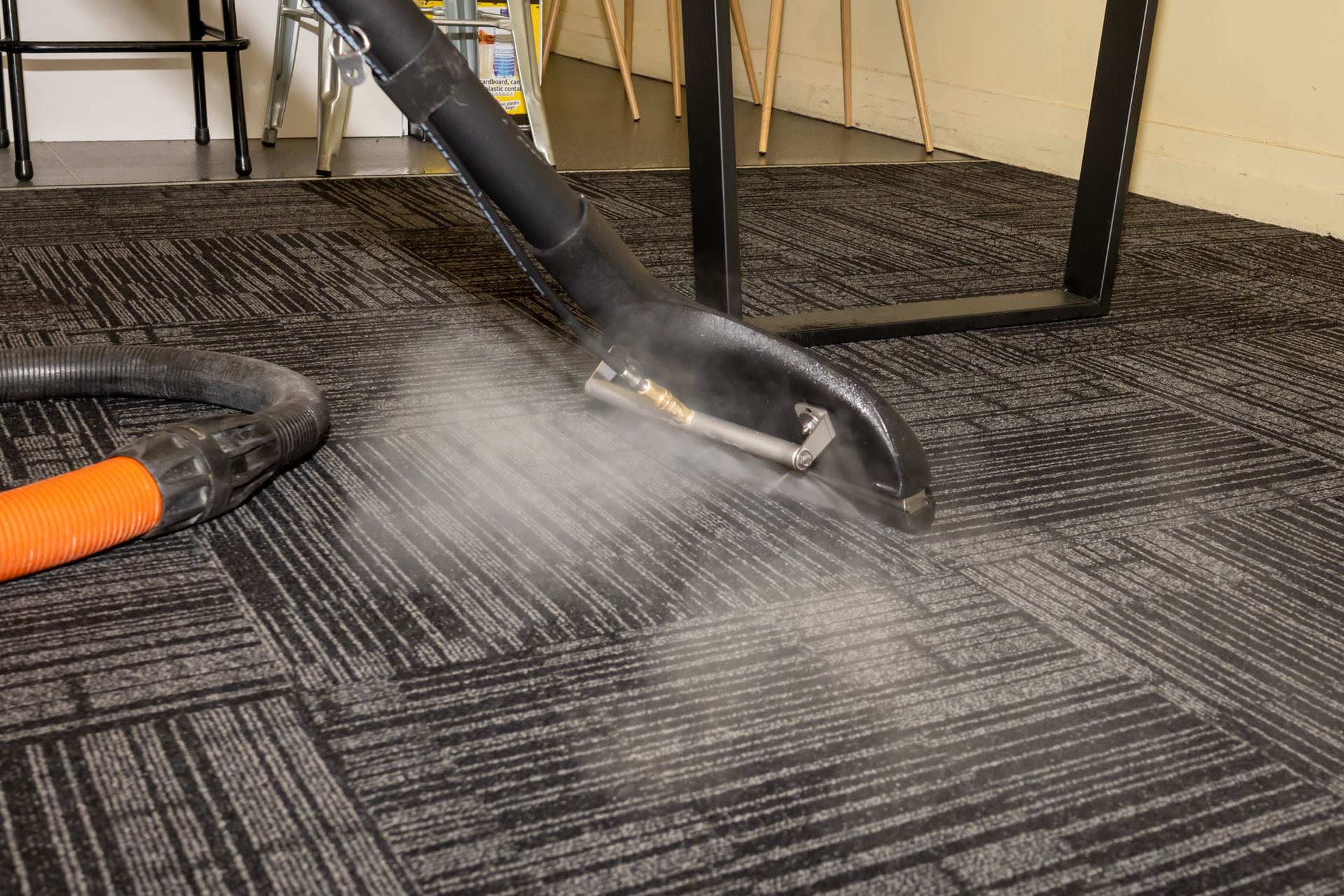 A steam carpet cleaning wand extracting soil from dark commercial office carpet tiles