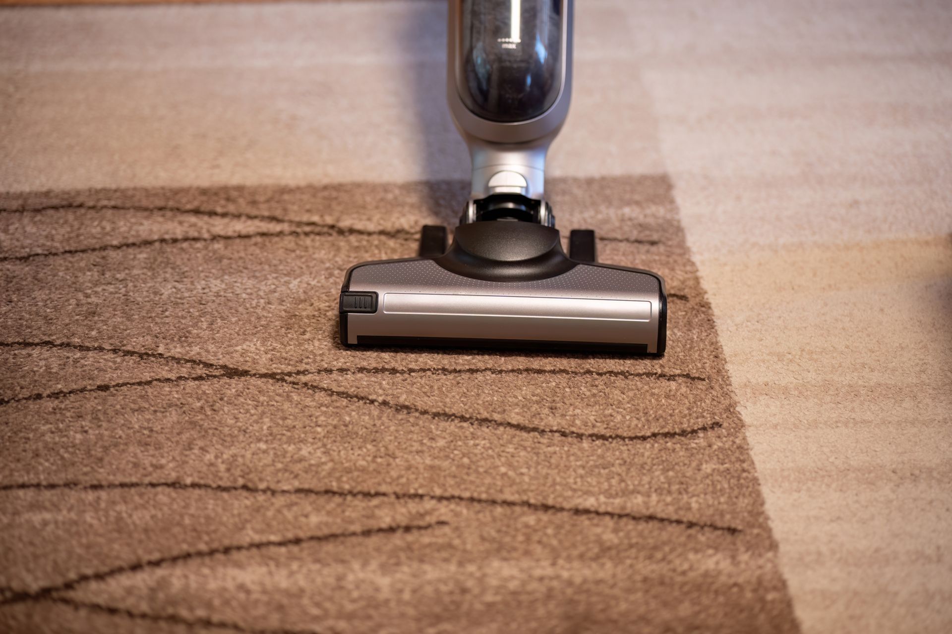 Vacuum cleaner head on a beige carpet, cleaning a section with visible dirt lines