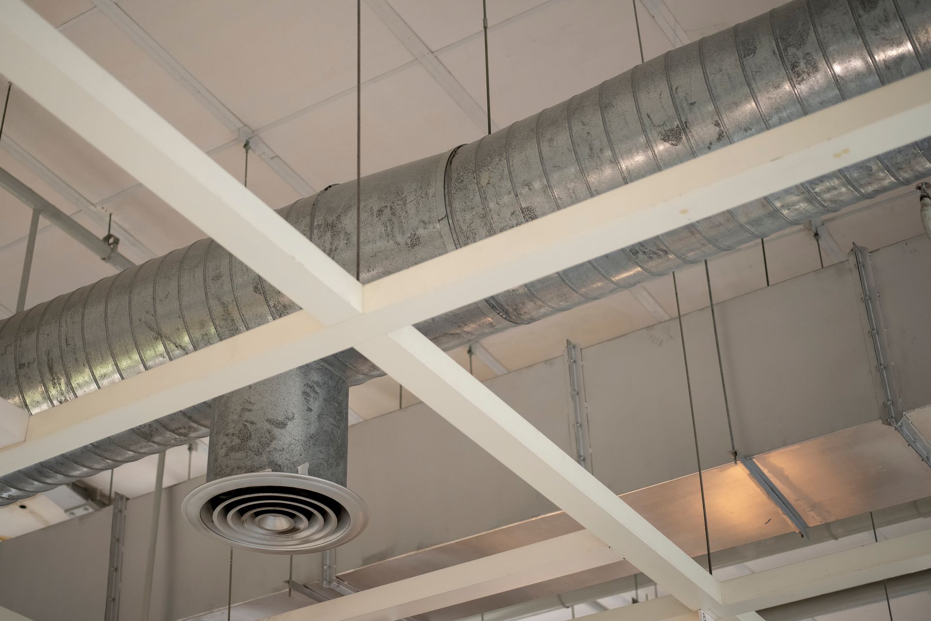 Metal ductwork and white beams on a white ceiling. HVAC air vent visible.