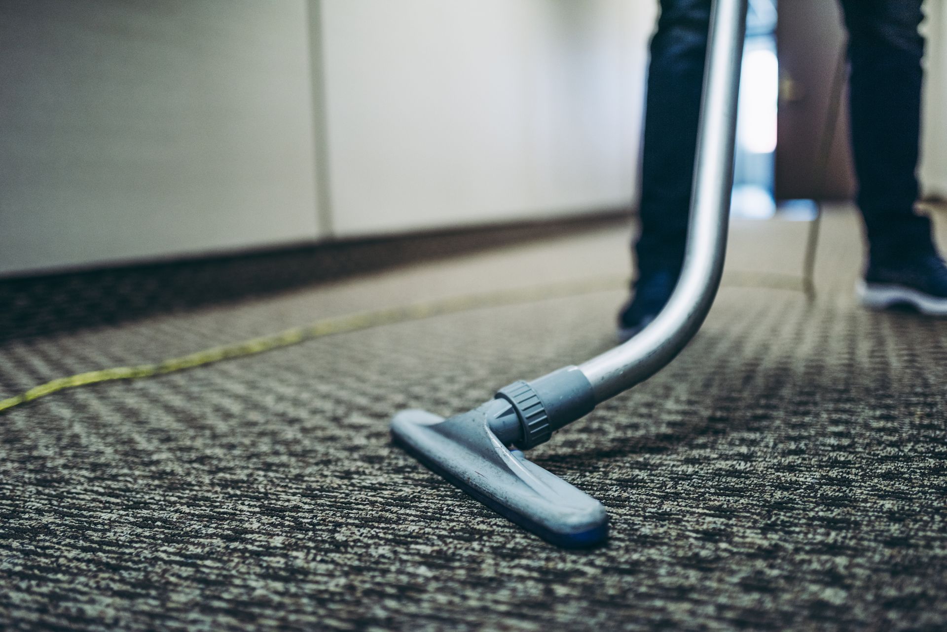 Person vacuuming a carpeted floor, silver vacuum head close to the carpet.