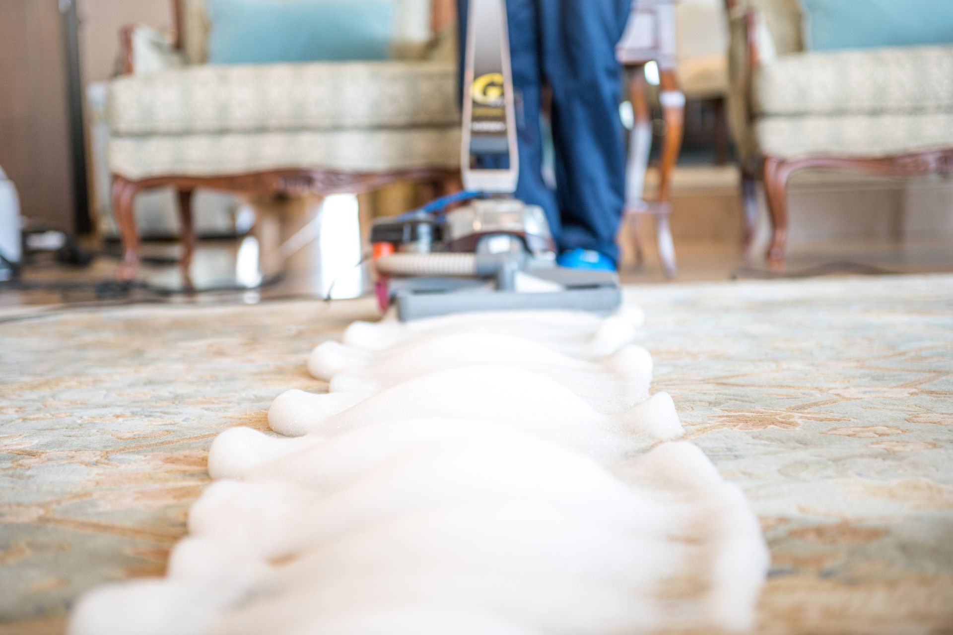 A professional carpet cleaning machine applying foam on a living room rug.