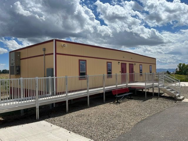 Tan modular beige building with white wheelchair ramp and railings under a cloudy sky.