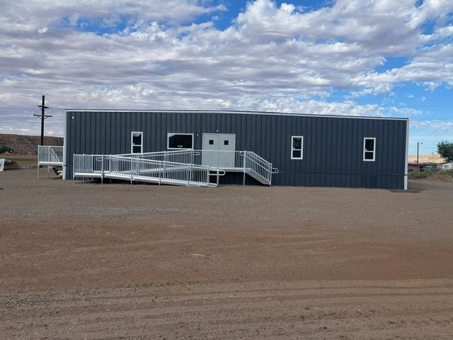 Blue portable building with wheelchair ramp in a gravel lot under a cloudy sky