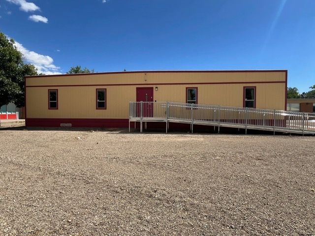 Single-story tan building with a ramp on a gravel lot under a clear blue sky