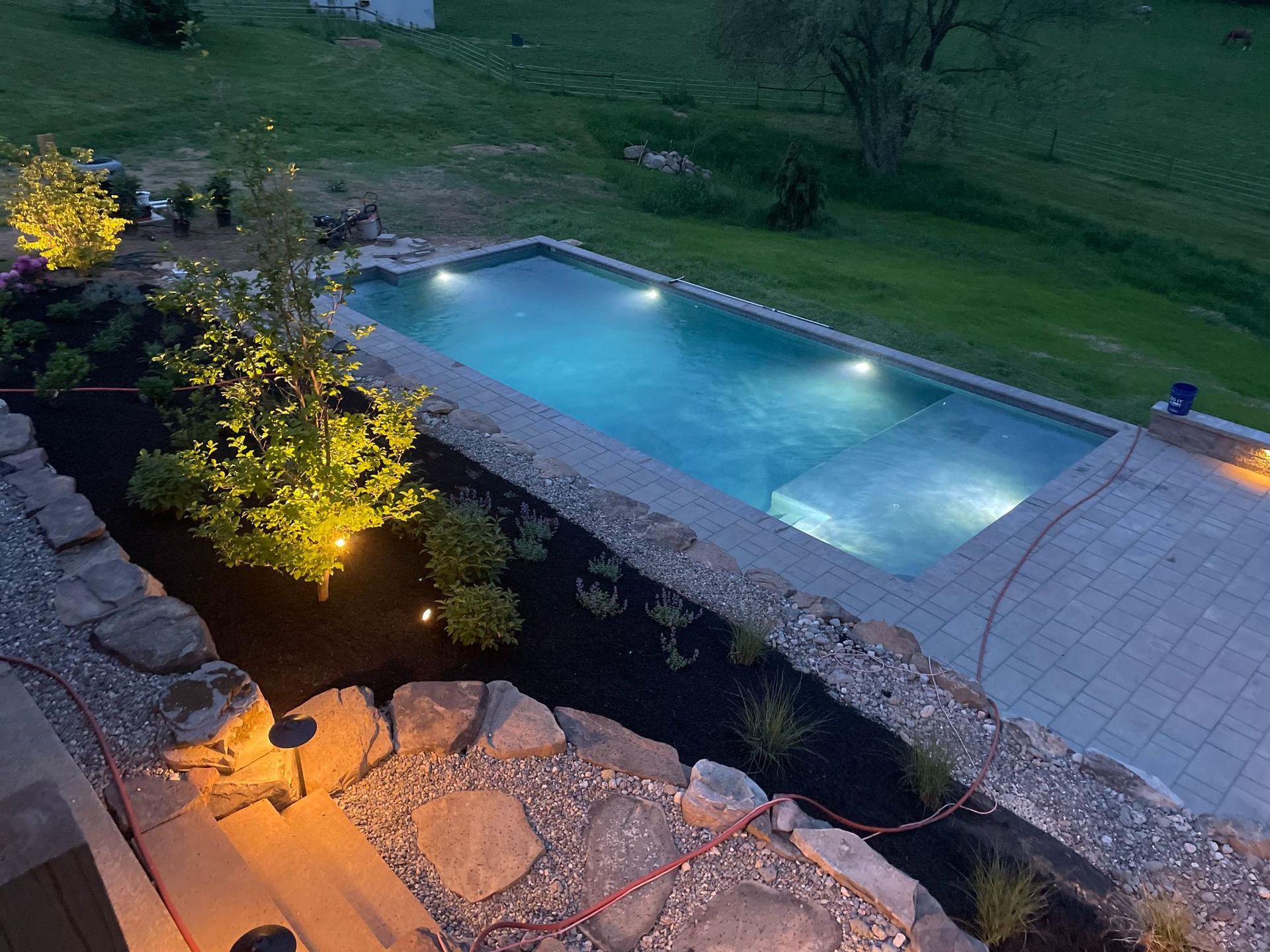 Custom lit swimming pool with paver surround at dusk