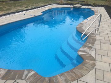 High-angle view of a backyard featuring a new paver patio surrounding a kidney-shaped pool at sunset.