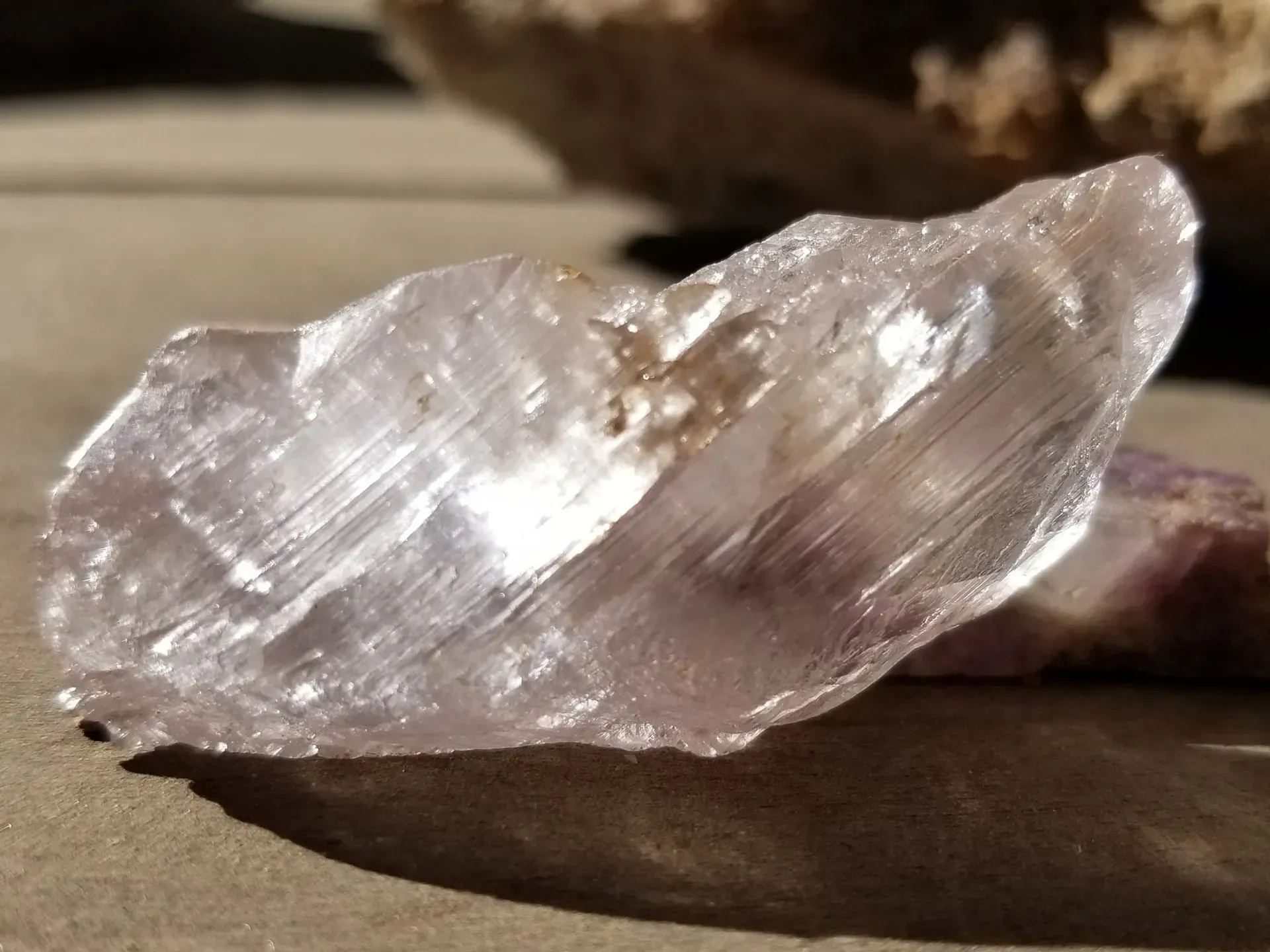 Clear, translucent crystal shard on a surface, reflecting light.