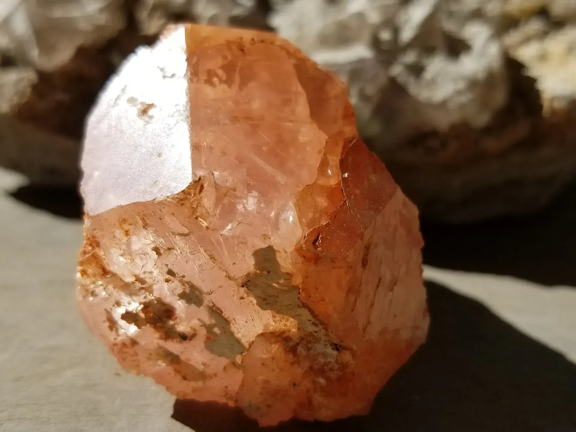 Orange-pink translucent crystal with rough edges on a flat surface