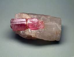 Pink crystal embedded in a rough gray rock on a plain background
