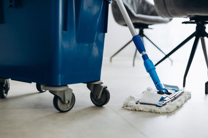 Mop cleaning a white floor beside a blue janitorial cart with wheels