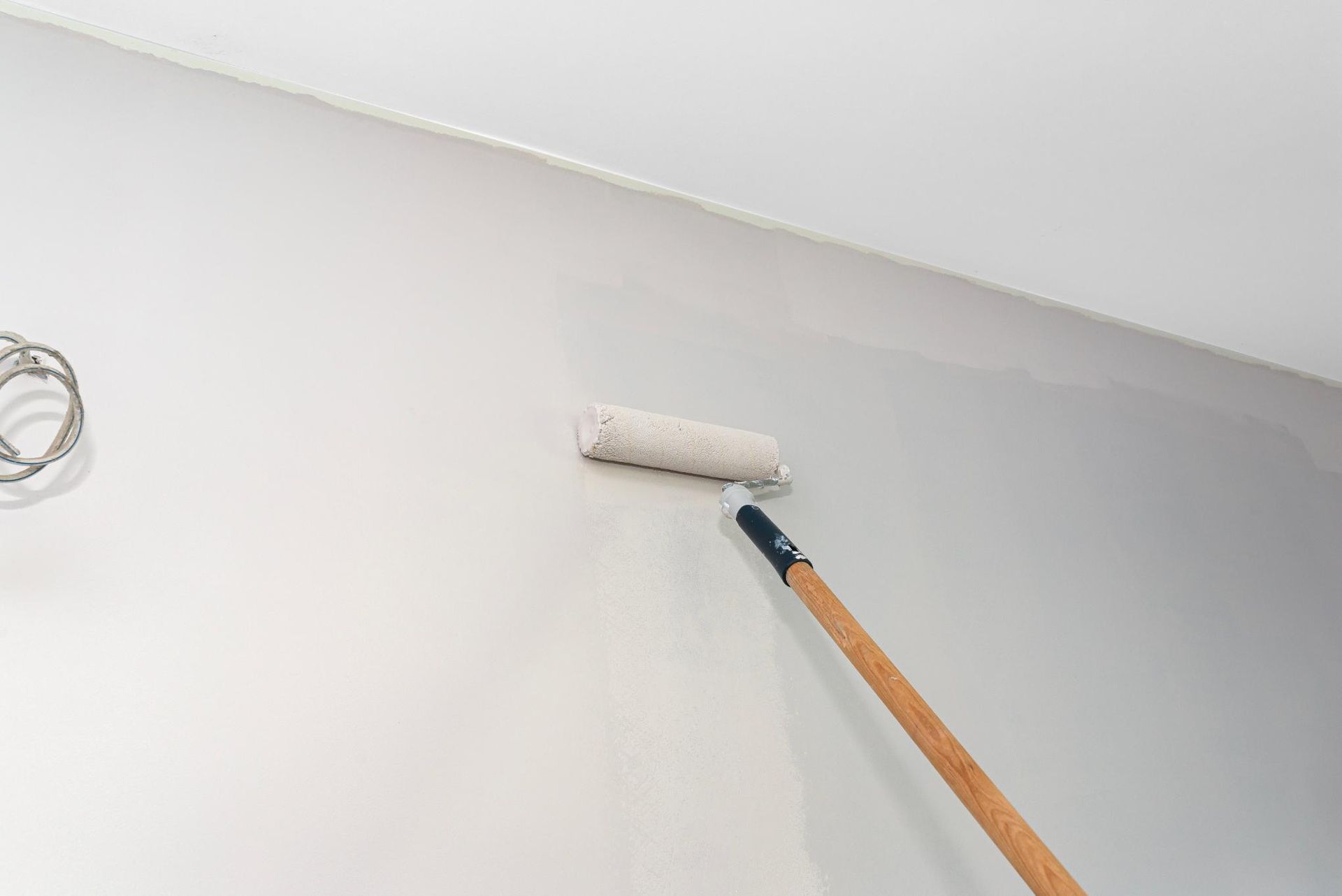 Paint roller applying white paint to a wall near the ceiling.