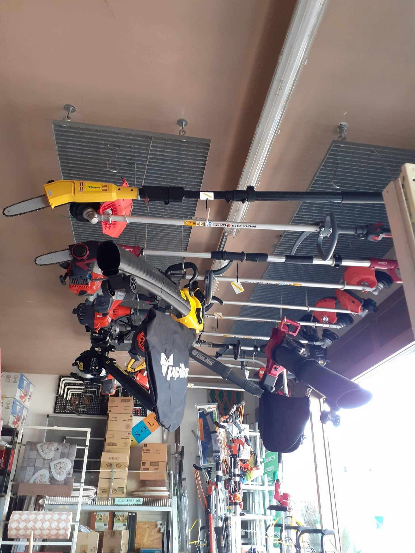 Corridoio interno di un negozio con attrezzi appesi, tra cui elettroutensili rossi e gialli esposti su appositi scaffali.