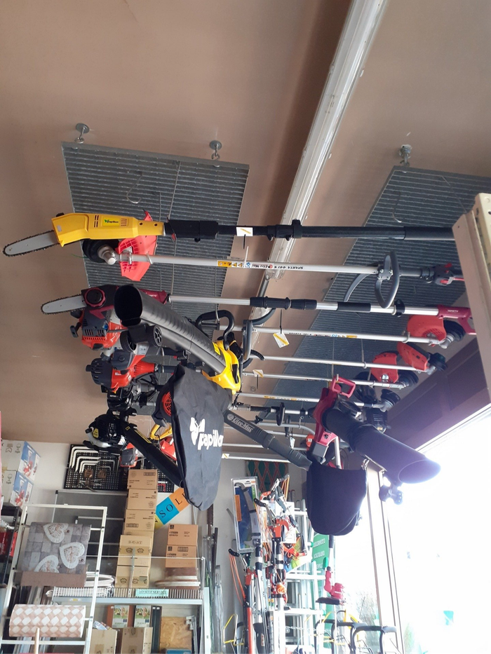Corridoio interno di un negozio con attrezzi appesi, tra cui elettroutensili rossi e gialli esposti su appositi scaffali.