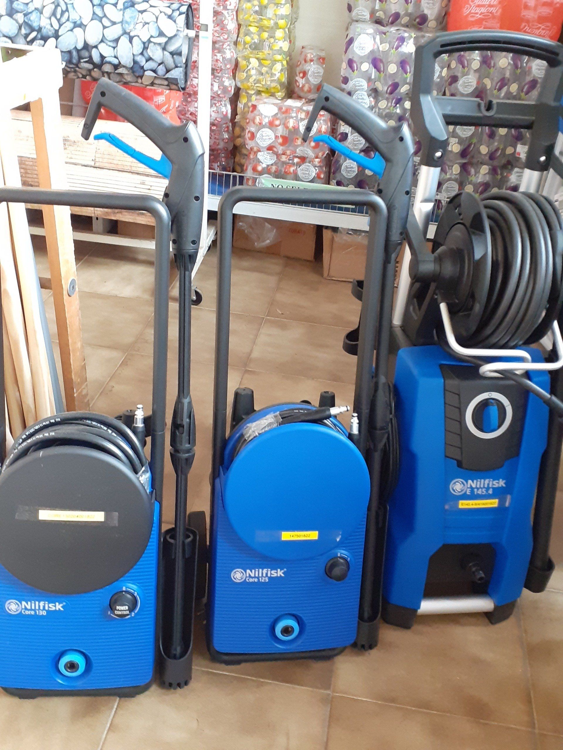 Tre idropulitrici blu, con tubi e maniglie neri, posizionate in verticale in un espositore di un negozio.