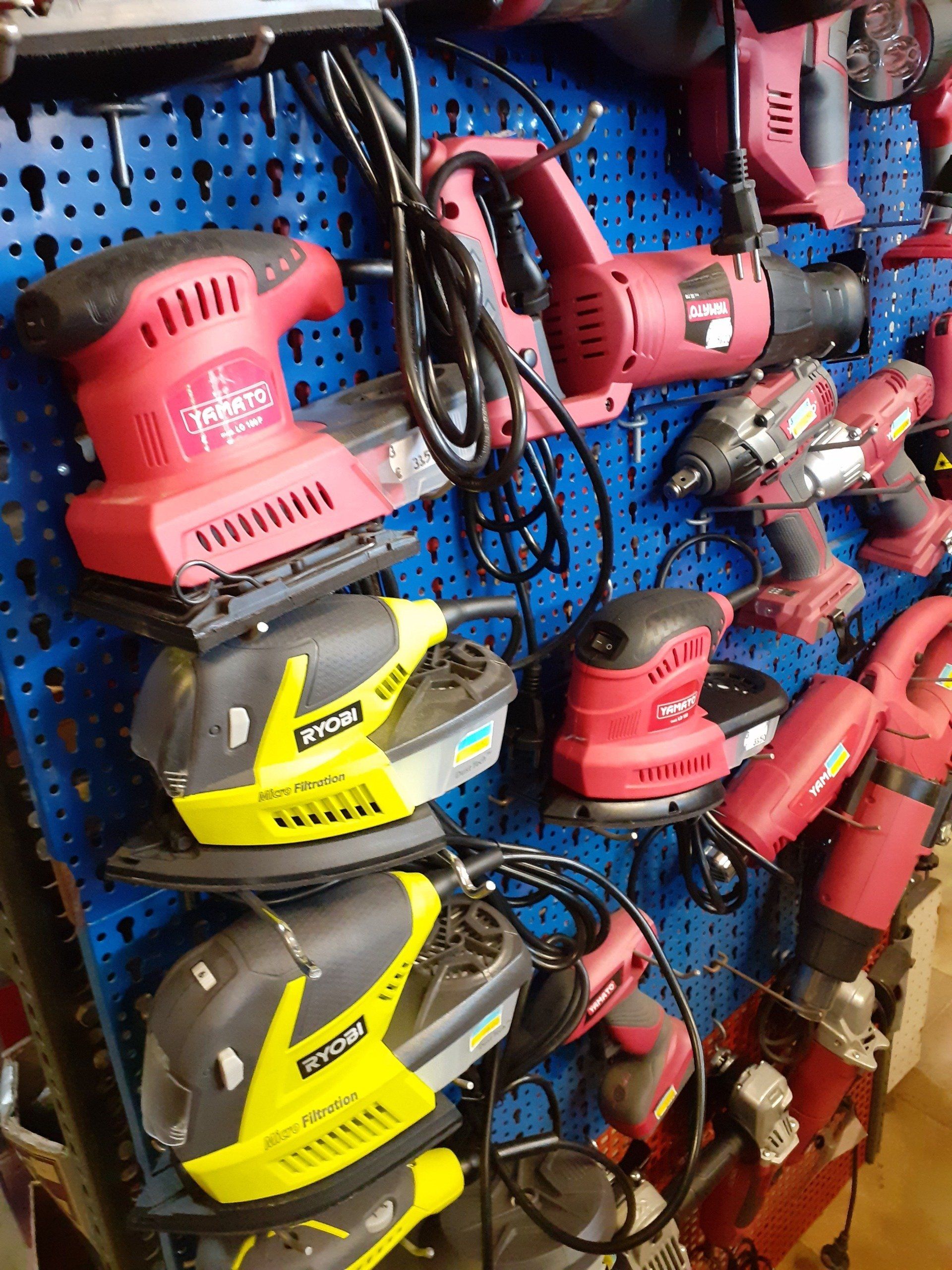 Parete di utensili elettrici e trapani appesi, di colore rosso, nero e giallo, su un pannello forato blu.