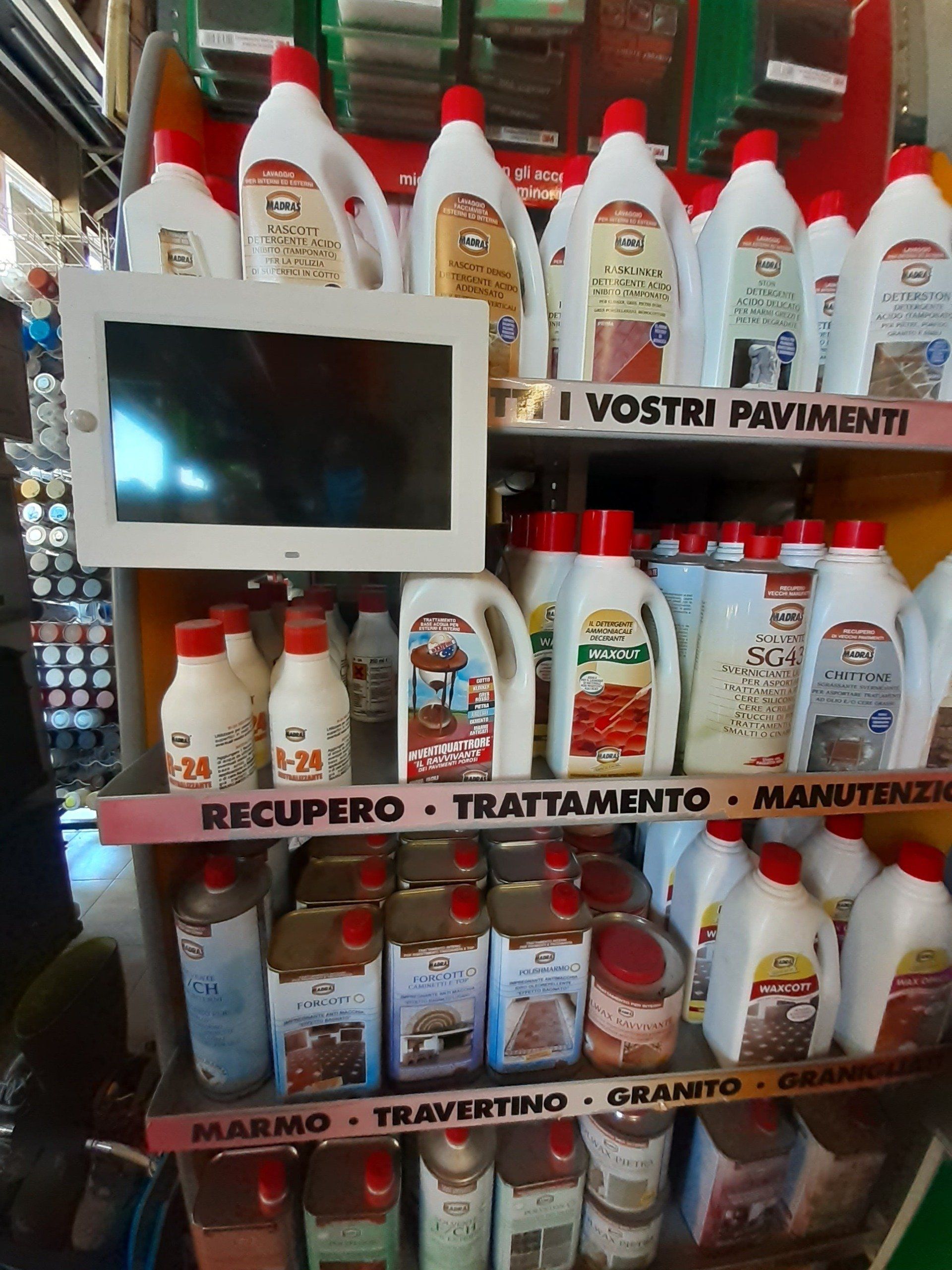 Prodotti e soluzioni per la pulizia sugli scaffali con etichette italiane, oltre a un piccolo monitor montato in un espositore del negozio.