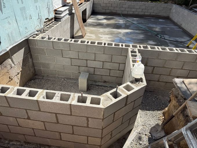 A bricklayer in gloves using a trowel to apply mortar on red bricks, constructing a wall.