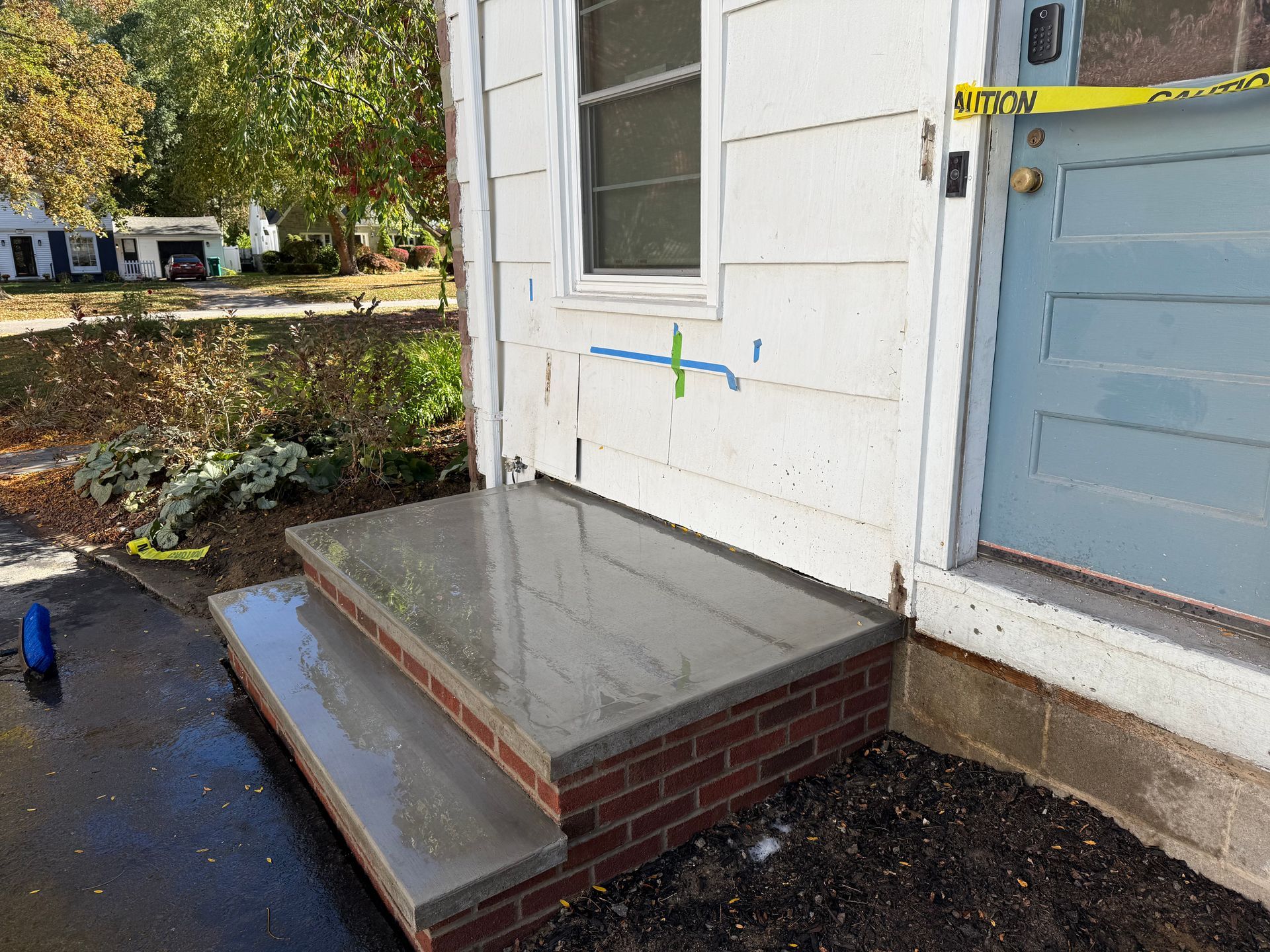 Newly poured concrete steps with brick siding leading to a house entrance with yellow caution tape across the door.