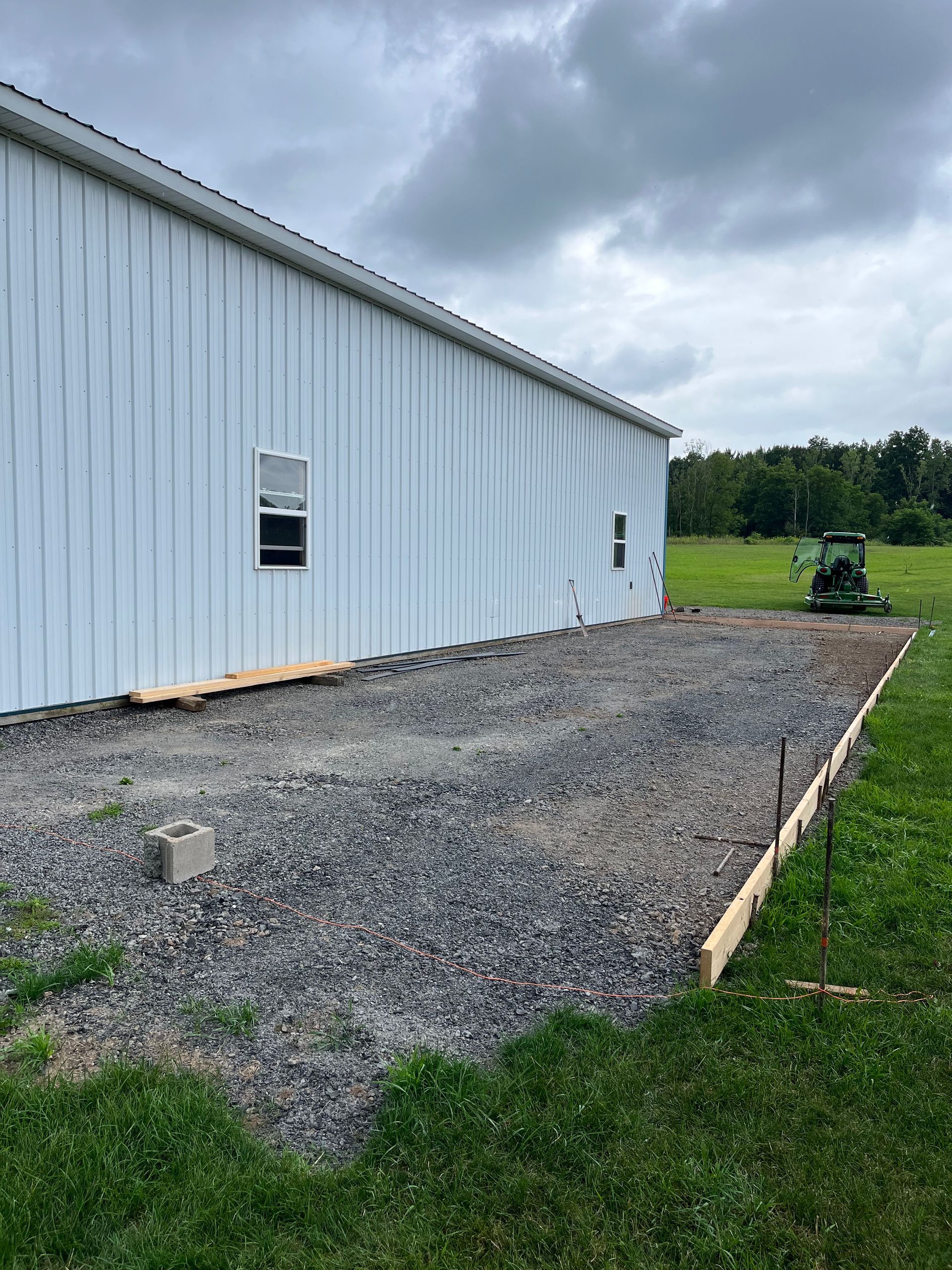 A white metal building with windows beside a gravel-filled foundation area being prepared for a concrete pour.