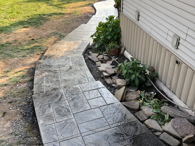 Stone pathway with geometric pattern through grassy area and trees.