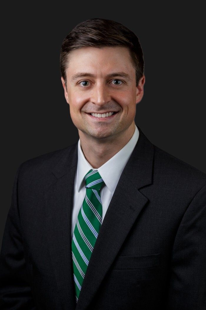Portrait of a smiling man in a dark suit with a green striped tie on a dark background