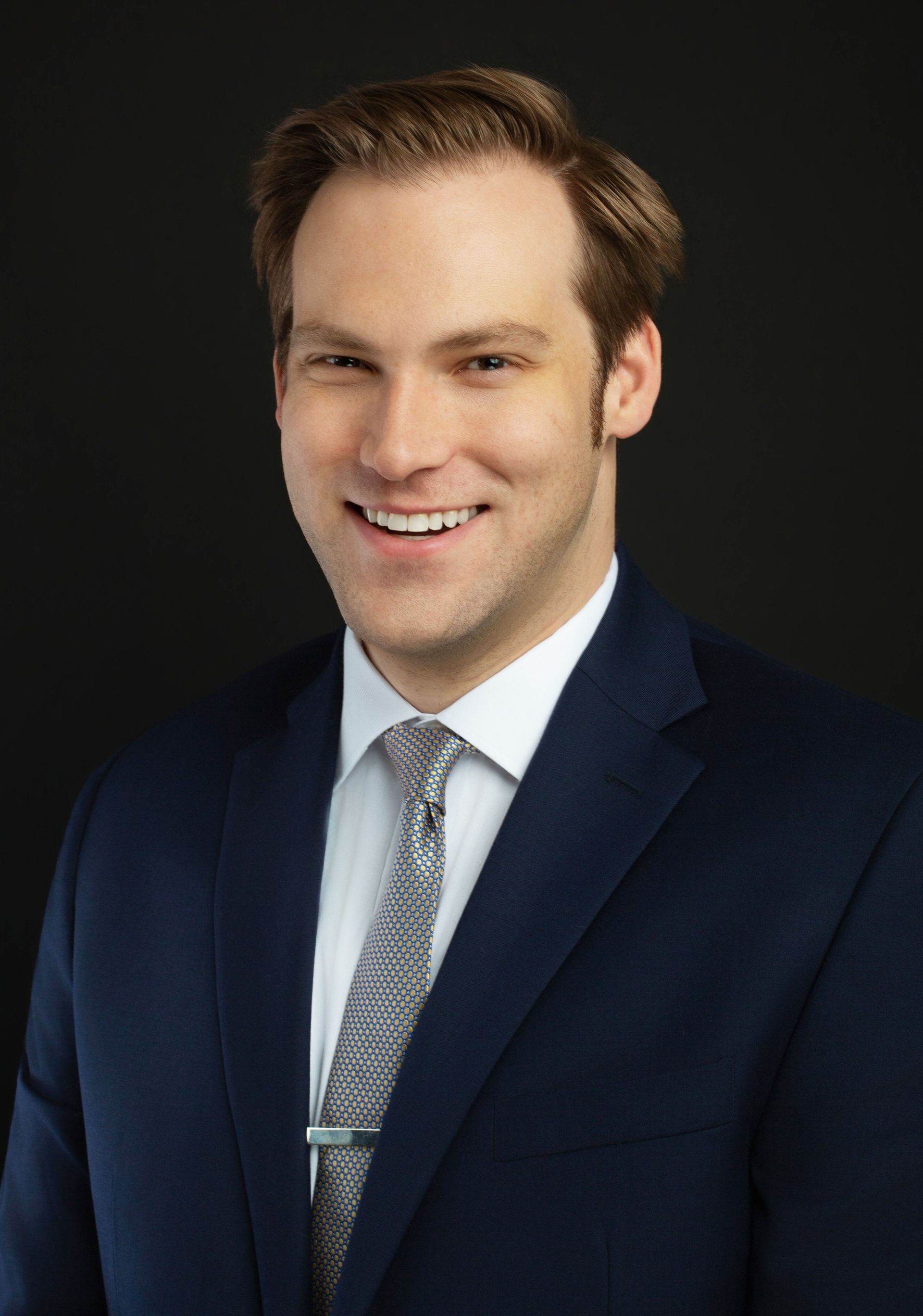 Matt Wayne Grant Konvalinka & Harrison P.C Studio portrait of a man in a gray suit, red patterned tie, and white pocket square against a dark background