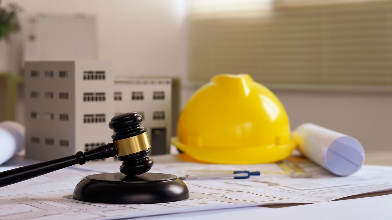 Architectural model with a yellow hard hat, gavel, and rolled plans on blueprints