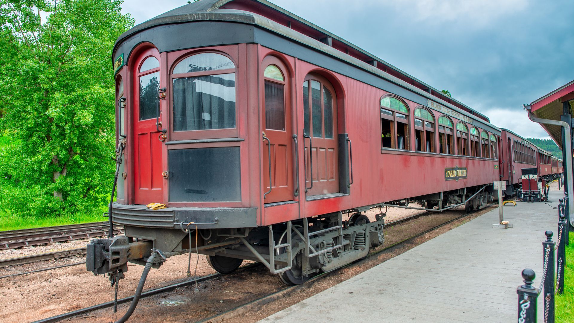 Vintage red passenger train car on tracks at a station platform under a cloudy sky